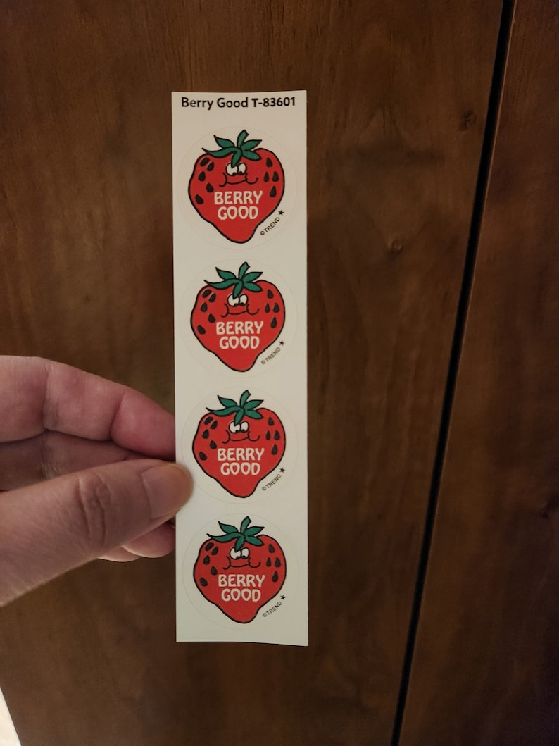 May include: A strip of four stickers featuring a smiling red strawberry with green leaves. Each sticker has the words "BERRY GOOD" and a star logo. The text "Berry Good T-83601" is printed at the top.