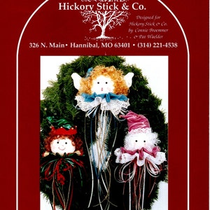 May include: A Christmas wreath with three handmade angel ornaments. The angels have curly hair, fabric faces, and are adorned with ribbons, lace, and beads. The text "Hickory Stick & Co." is at the top of the image.