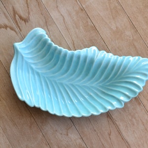 May include: A light blue ceramic leaf-shaped serving dish. The dish has a ribbed texture and is perfect for serving snacks or appetizers.