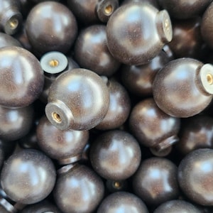 May include: A close-up shot of a pile of dark brown wooden knobs. Each knob is spherical with a cylindrical base and a threaded insert for attachment. The knobs have a smooth, polished finish, and the hardware is visible.
