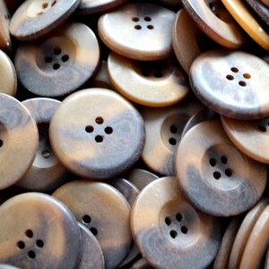 May include: A pile of brown and black buttons with four holes each. The buttons are made of a textured material and have a slightly raised edge.