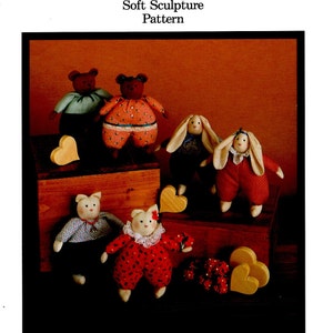 May include: A set of five handmade soft sculpture toys, including two bears, two bunnies, and a cat. The toys are dressed in colorful patterned fabric and have embroidered facial features. The toys are arranged on a wooden surface with heart-shaped wooden decorations.