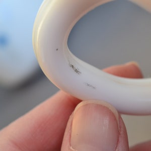May include: Close-up of a white plastic ring with two small black marks on the inside of the ring.