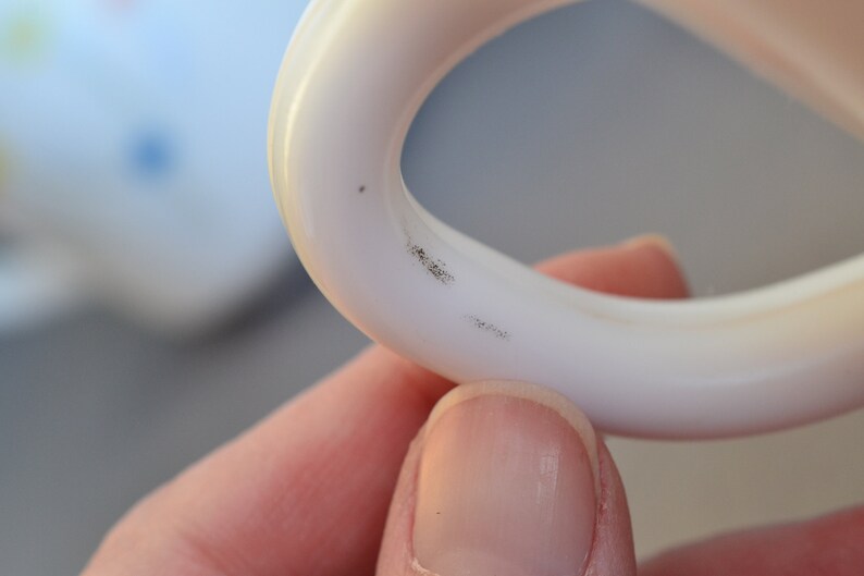 May include: Close-up of a white plastic ring with two small black marks on the inside of the ring.