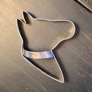 May include: A silver metal cookie cutter shaped like a horse's head. The cutter has a simple design with a rounded head and a flat, straight neck.