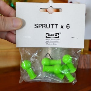 May include: A pack of six green plastic hooks labelled "SPRUTT x 6" with the IKEA logo and the text "Design and Quality IKEA of Sweden Made in China".