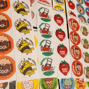 May include: A collection of vintage stickers with various designs. The stickers feature images of a bee with the text "BEE-UTIFUL!", a lawnmower, a strawberry with "BERRY GOOD", and a mug of beer with "COOL".