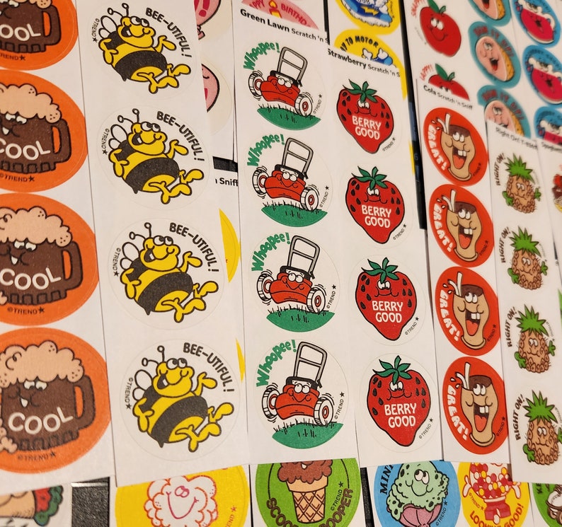 May include: A collection of vintage stickers with various designs. The stickers feature images of a bee with the text "BEE-UTIFUL!", a lawnmower, a strawberry with "BERRY GOOD", and a mug of beer with "COOL".