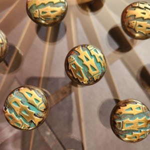 Peut inclure: Gros plan de plusieurs boutons de meuble antiques de couleur laiton avec un motif turquoise et or. Les boutons ont une forme circulaire et sont disposés en motif. Le motif semble être abstrait.