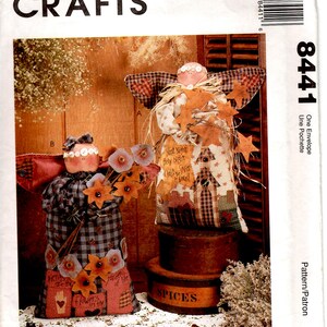 May include: Two handmade fabric angels, one with a plaid dress and a bouquet of flowers, the other with a patchwork dress and a halo of straw and leaves. Both angels are sitting on wooden boxes with the words "SPICES" and "Garden of Life" printed on them.