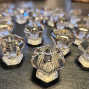 May include: A group of clear glass drawer pulls with a faceted design. The pulls are arranged in a random pattern on a dark surface.