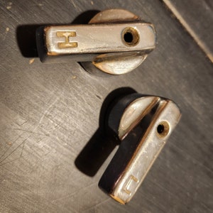 May include: Two silver metal knobs with a black base. The knobs have a small hole in the centre and a letter on the side. The top knob has the letter "H" and the bottom knob has the letter "C".