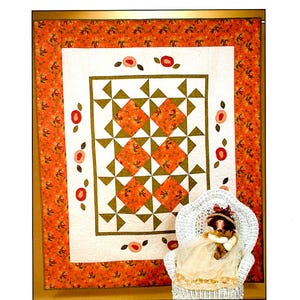 May include: A quilt with a white background and a central design of orange and green squares and triangles. The quilt is surrounded by a border of orange fabric with a floral pattern. A white wicker chair with a doll sitting in it is in the foreground.
