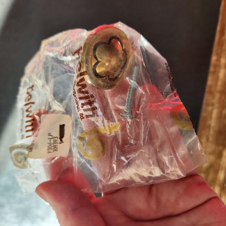 May include: A gold-colored cabinet knob with a decorative clover design, packaged with two screws. The package is labeled "Telwith International Ltd."