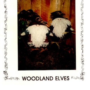 May include: Two woodland elf dolls with white yarn beards and brown felt hats. The dolls are wearing red and white patterned shirts and brown pants. The dolls are sitting on a brown wooden surface. The image is titled "Woodland Elves" and "Ginger Snap Junction".