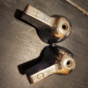 May include: Two chrome-plated faucet handles with a round shape and a flat, rectangular base. The handles have a letter 'H' and 'C' engraved on them.