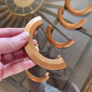 Peut inclure: Un ensemble de cinq poignées de porte de placard de couleur or en forme de C. Les poignées sont en métal lisse et arrondi.