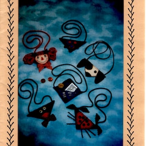 May include: Five felt penny pocket or needle case necklace designs. The designs include a ladybug, a dog, a cat, a girl, and a pocket. The designs are on a blue background. ©2000 Vickie Clontz Annie's Keepsakes.
