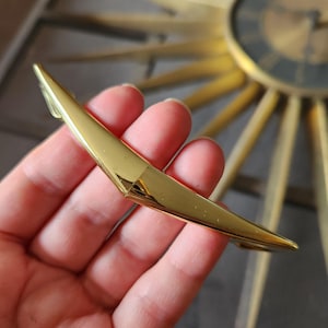 May include: A gold-toned metal cabinet door handle with a pointed, angular design.