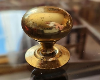 May include: A vintage brass doorknob with a round, ball-shaped handle and a circular base. The brass has a warm, golden hue with signs of wear, suggesting age. The doorknob is set against a reflective surface.