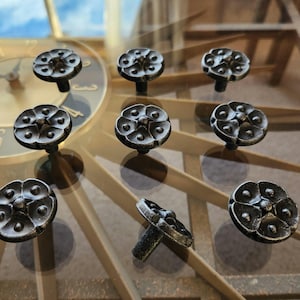 May include: Nine antique-style cabinet knobs with a dark bronze finish. Each knob features a floral design with a central raised element and a rounded base. The knobs are arranged on a reflective surface.