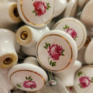May include: White ceramic cabinet knobs with a gold trim and a pink rose design. The knobs have a screw for easy installation and are ideal for adding a touch of elegance to furniture or cabinets.