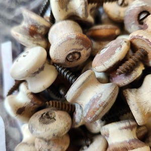 May include: A close-up of a pile of vintage wooden drawer pulls with a distressed white paint finish. The pulls have a variety of shapes and sizes, and some have screws attached.