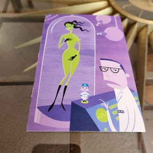 May include: A vibrant art print depicting a green alien woman in a glass case, a scientist, and a small baseball figure. The print has a purple background and a retro cartoon style.