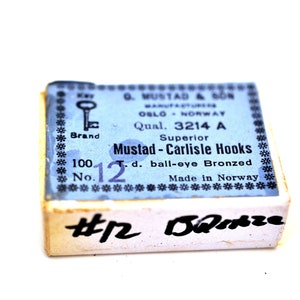 May include: A blue and white box of Mustad - Carlisle Hooks, size 12, ball-eye bronzed. The box is labeled "Superior" and "Made in Norway".