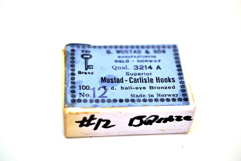 May include: A blue and white box of Mustad - Carlisle Hooks, size 12, ball-eye bronzed. The box is labeled "Superior" and "Made in Norway".