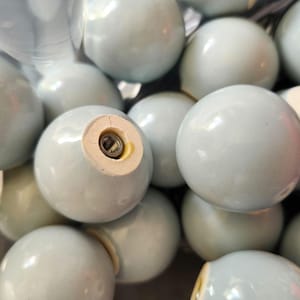 May include: A close-up of several pale blue ceramic cabinet knobs. Each spherical knob has a glossy finish. One knob shows a metal screw for fixing. The knobs are grouped together, possibly for a bulk purchase or storage.