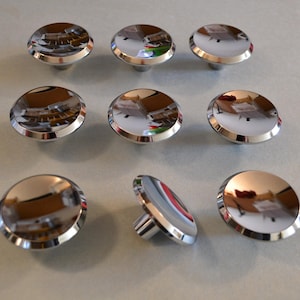 May include: Nine chrome cabinet knobs with a round, slightly domed top and a raised edge. The knobs have a shiny, reflective finish.