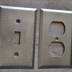 May include: Two brushed nickel wall plates with a textured finish. One plate has a single light switch opening and the other has a double outlet opening.