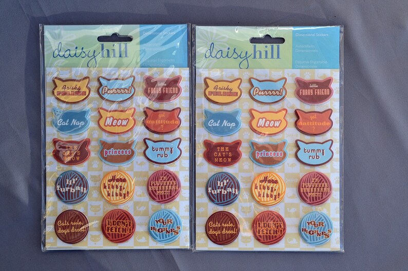 May include: Two packages of cat-themed decorative stickers. Each package contains 18 stickers with various cat-related phrases and images, including "Cat Nap", "Meow", "The Cat's Meow", "Princess", "Tummy Rub", "Furball", "Cats Rule, Dogs Drool", and "I Don't Fetch".