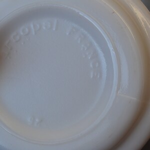 May include: Close-up of the bottom of a white ceramic mug with the words "Copal  France" embossed on the bottom.