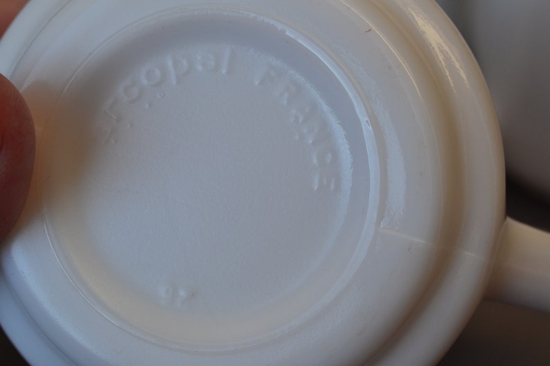 May include: Close-up of the bottom of a white ceramic mug with the words "Copal  France" embossed on the bottom.
