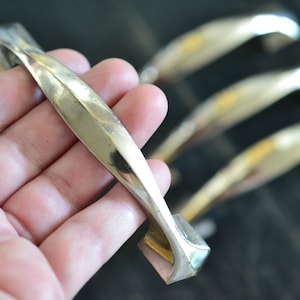May include: Four silver cabinet door handles with a curved design. The handles are in a hand, with the closest handle in focus.