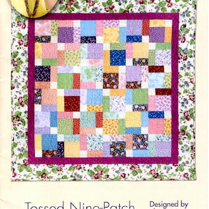 Peut inclure: Une courtepointe colorée avec un motif en neuf carrés. La courtepointe est composée de carrés de différentes couleurs et motifs, notamment rose, bleu, jaune, vert et violet. La courtepointe est entourée d'une bordure en tissu rose à motif floral.