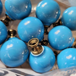 Peut inclure: Ensemble de boutons de meubles sphériques bleu clair avec des bases en laiton vieilli. Les boutons sont brillants et espacés uniformément, suggérant un ensemble pour meubles ou décoration. Les bases en laiton ont un design orné.