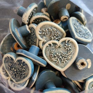 May include: A collection of blue and white decorative cabinet knobs. The knobs have a variety of shapes, including hearts and ovals, and feature floral designs. The knobs are made of a ceramic-like material.