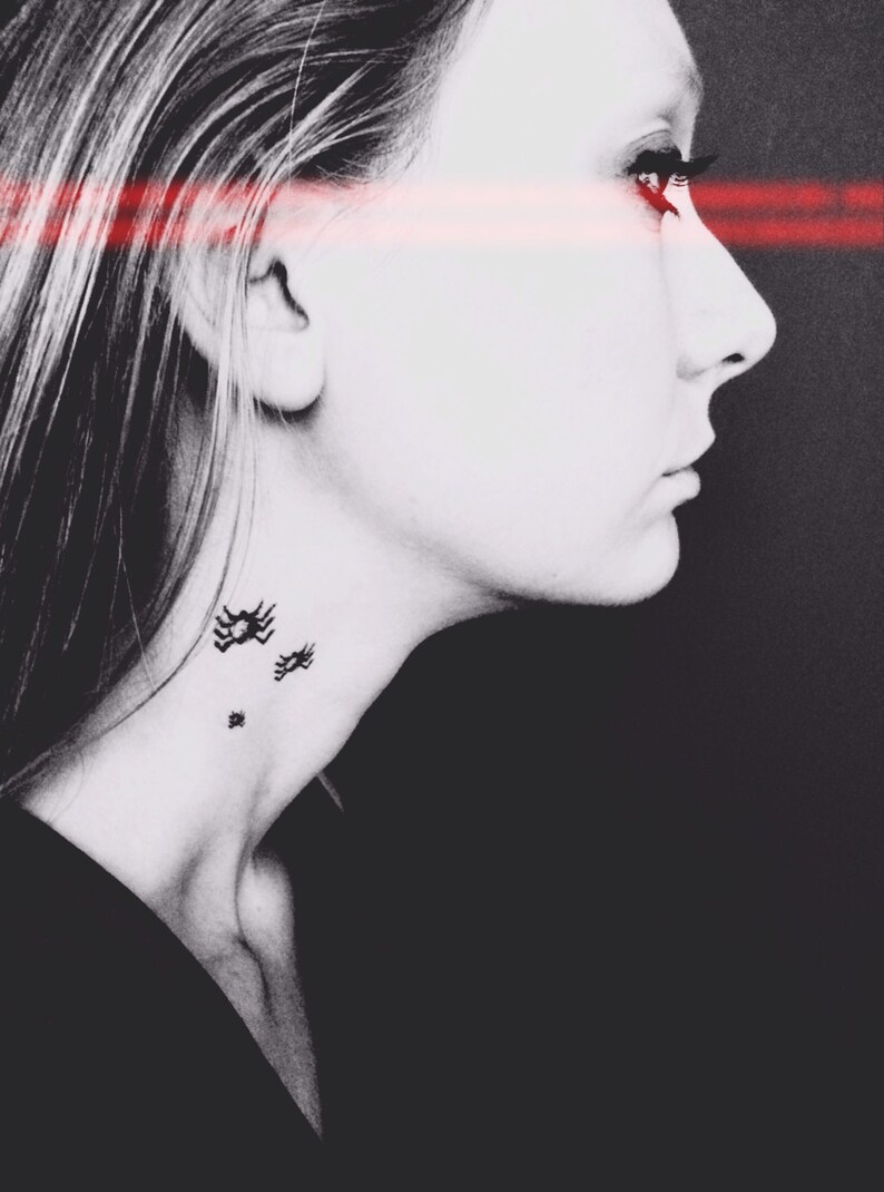 May include: A black and white profile portrait of a person with three small black spider tattoos on the side of the neck. A horizontal red light beam crosses the eyes, creating a high-contrast effect against the dark background.