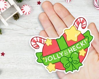 May include: A red and green Christmas sticker with a candy cane, a bow, and stars. The sticker says "Jolly as Heck!"