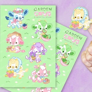 May include: A sheet of stickers featuring cute cartoon cows with different colored spots and accessories. The cows are holding various items like flowers, fruit, and a slice of toast. The stickers are on a green background with white flowers. The text "GARDEN COWS BY BRIGHT BAT DESIGN" is at the top of the sheet.