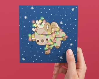 May include: A blue Christmas card with a cartoon reindeer tangled in Christmas lights. The reindeer is brown with a white face and has a red nose. The lights are green, red, and yellow.