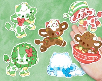 May include: Set of six festive cow stickers with different holiday themes. The stickers feature a cow wearing a wreath, a cow with a candy cane, a cow with a chocolate and sprinkles topping, a cow with a Santa hat, a cow with a cup of hot chocolate, and a cow with a blue bow.