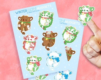 May include: A set of nine winter-themed cow stickers. The stickers feature cows wearing winter accessories like wreaths, candy canes, and Santa hats. The stickers are on a light blue background with snowflakes.