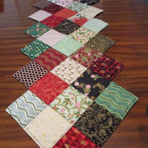 May include: A quilted table runner with a diamond pattern. The runner features various fabrics in red, green, gold, and black, with floral, geometric, and holiday-themed designs. The date "09/17/2025" is visible on the bottom right corner.