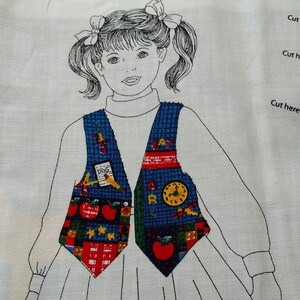 May include: A fabric panel featuring a sketched outline of a girl wearing a vest. The vest is decorated with colorful school-themed patterns, including apples, a clock, and the letters "A" and "B". The panel is on a white background.
