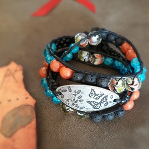 May include: A multi-strand bracelet featuring black lava rock beads, turquoise and orange glass beads, and a silver charm with two butterflies and floral designs.