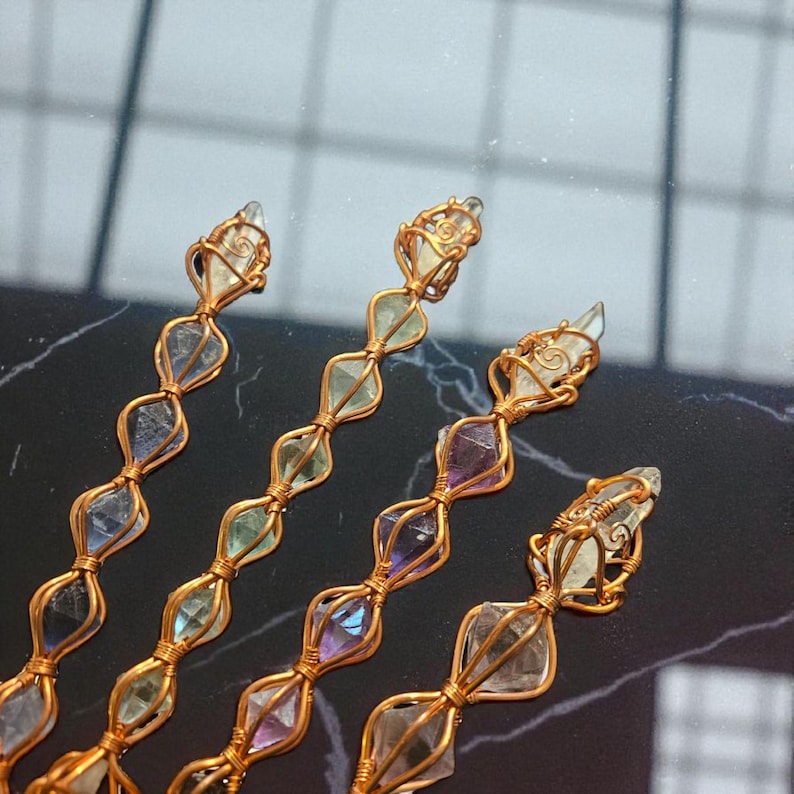 May include: Four vertical strands of wire-wrapped crystals featuring copper-colored metal wire coiled around individual translucent stones. The stones display various hues including pale green, light purple, and clear, arranged in a repeating pattern.